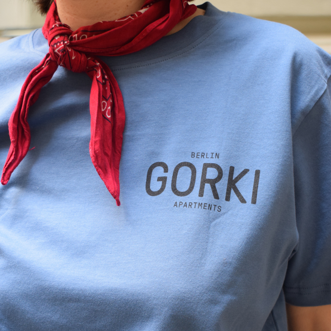 Blaues T-Shirt mit dem GORKI Logo auf der Vorderseite und unsere Fassade auf der Rückseite